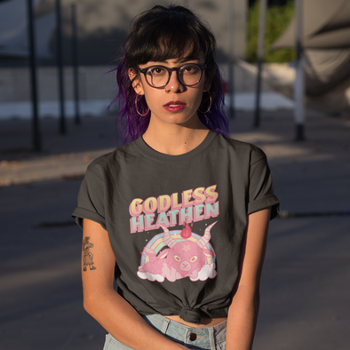 woman wearing a shirt that says godless heathen with a cute pink baphomet sitting by a rainbow